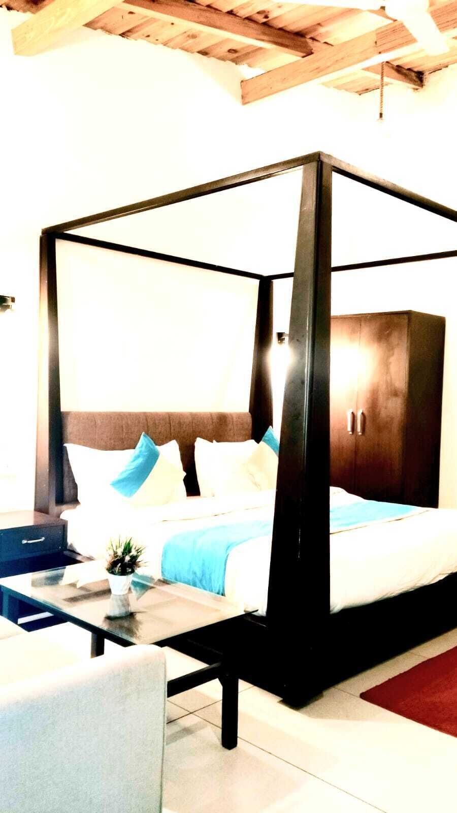 Un llit amb cortines, amb un capçal de fusta, una petita taula de nit amb una planta i una catifa vermella al terra.