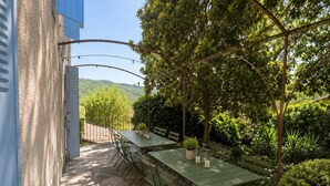 An outdoor dining area with a table and benches, surrounded by greenery and a view of hills. - Country house in the heart of the Ardèche, near Valence, with mountain views (Saint-Laurent-du-Pape)