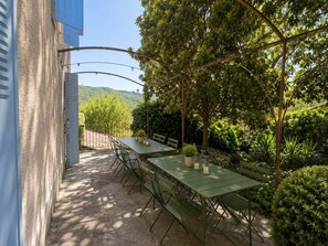An outdoor dining area with a table and benches, surrounded by greenery and a view of hills. - Country house in the heart of the Ardèche, near Valence, with mountain views (Saint-Laurent-du-Pape)