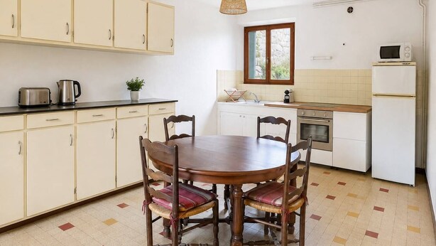 A kitchen with a dining table, chairs, cabinets, a stove, a microwave, and a hanging light fixture. - Country house in the heart of the Ardèche, near Valence, with mountain views (Saint-Laurent-du-Pape)