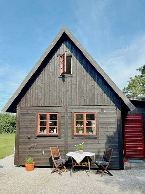 A wooden cabin with two windows, a red door, and a table with chairs outside. - Traditional Gotland log houses (Gotlands län)