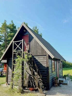 Une construction rustique en bois, dotée d’un toit à forte pente, d’une porte rouge et d’un escalier en bois menant à un porche.