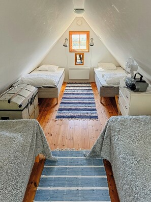 Une petite chambre mansardée avec deux lits, une fenêtre, un radiateur et un ventilateur.
