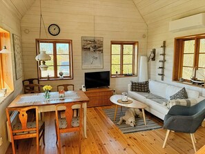 A cozy living room with wooden floors, a dining table, a sofa, and a television.
