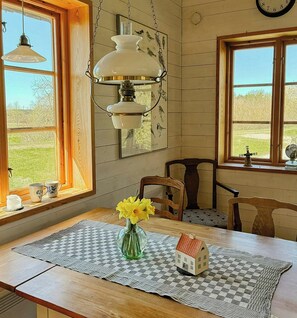 A dining area with a table set for two, a vase with flowers, and a small house model on a checkered placemat.