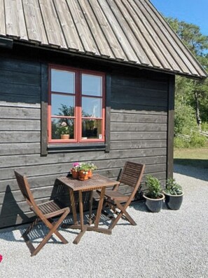 A wooden cabin with a red-framed window, a table with chairs, and potted plants. - Traditional Gotland log houses (Gotlands län)