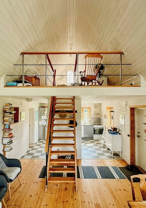 A loft-style room with a wooden staircase, a loft bed, and a kitchen area. - Traditional Gotland log houses (Gotlands län)