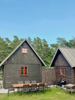 Two wooden cabins with red-framed windows, a dining table with chairs, and a barbecue grill.