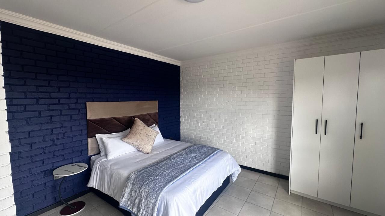 A bedroom with a bed, a bedside table, a wardrobe, and a brick-patterned wall.