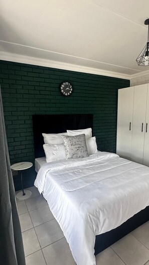 A bedroom with a bed, a round clock on the wall, a wardrobe, and a small round table.