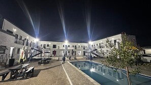 Un patio con piscina, mobiliario exterior y un edificio con varios balcones.