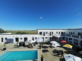 A hotel courtyard with a swimming pool, outdoor seating, and a building with multiple windows.