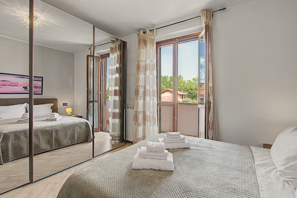 A hotel room with a bed, a nightstand, a lamp, a mirror, and a view of the outside.