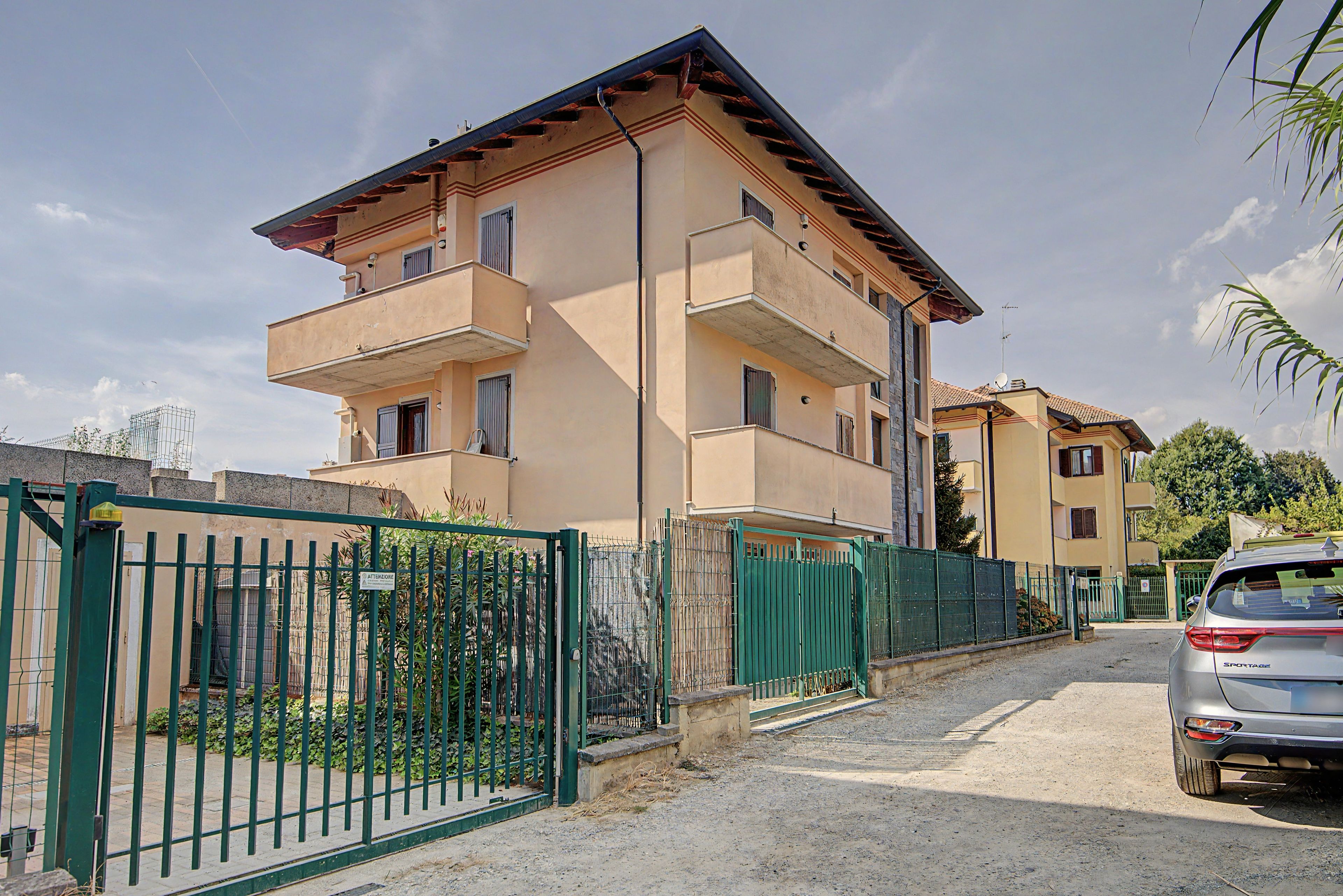 Un edificio residenziale a più piani con cancello automatico, un'auto parcheggiata e cielo sereno.