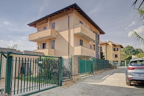 A multi-story residential building with a gated entrance, a parked car, and a clear sky.