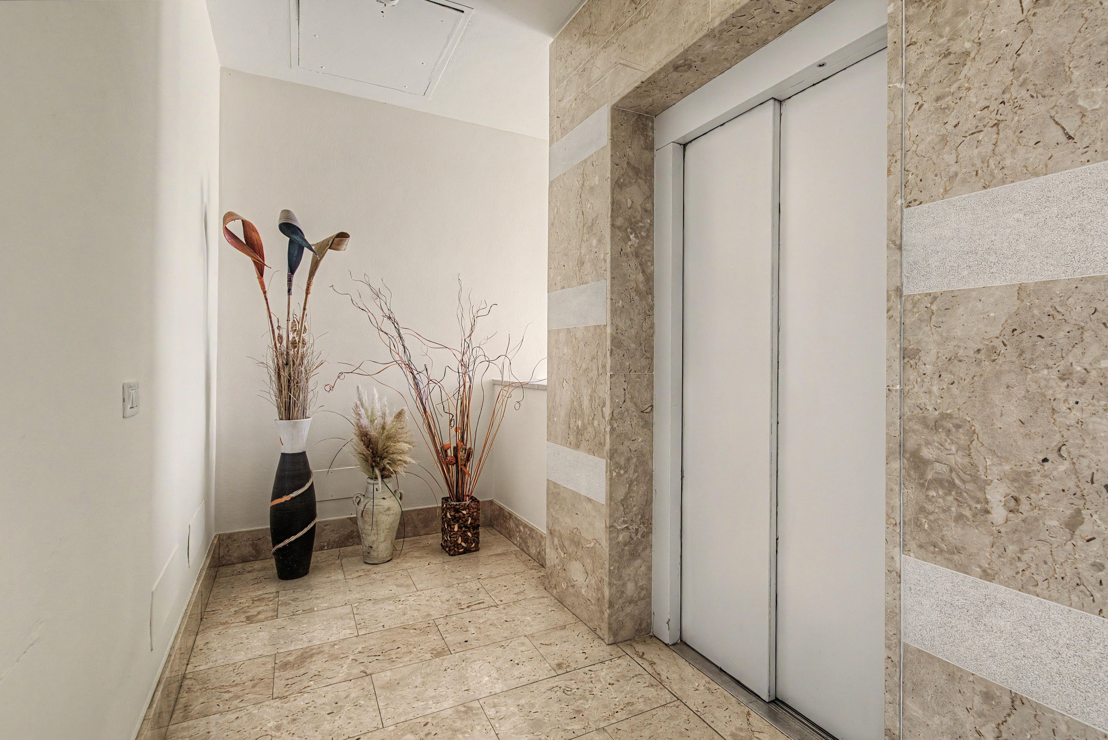 A hallway with a marble floor, a sliding door, and two vases with dried plants.