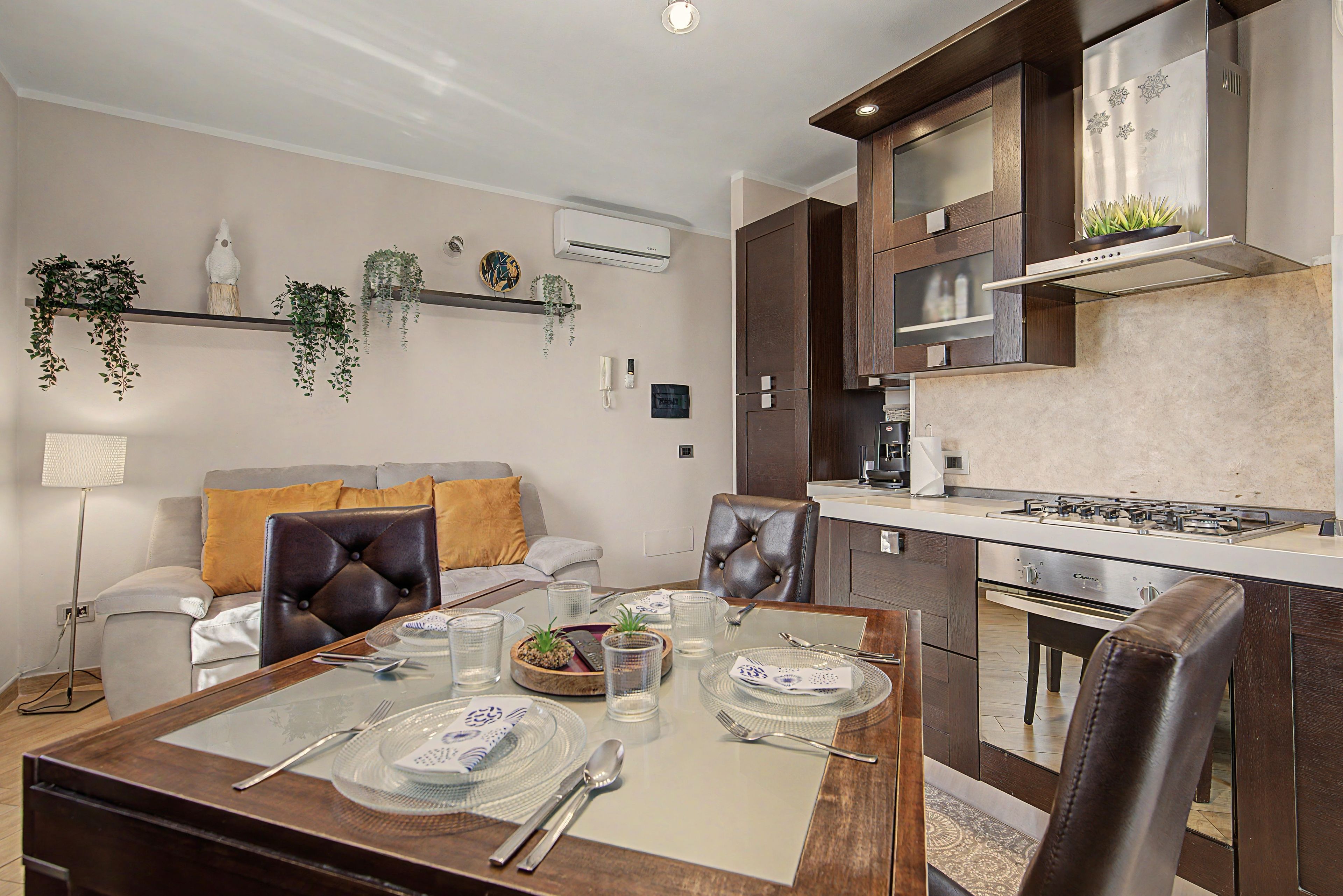 A modern kitchen with dark wood cabinets, a built-in stove, and a dining area with a glass table set for two.