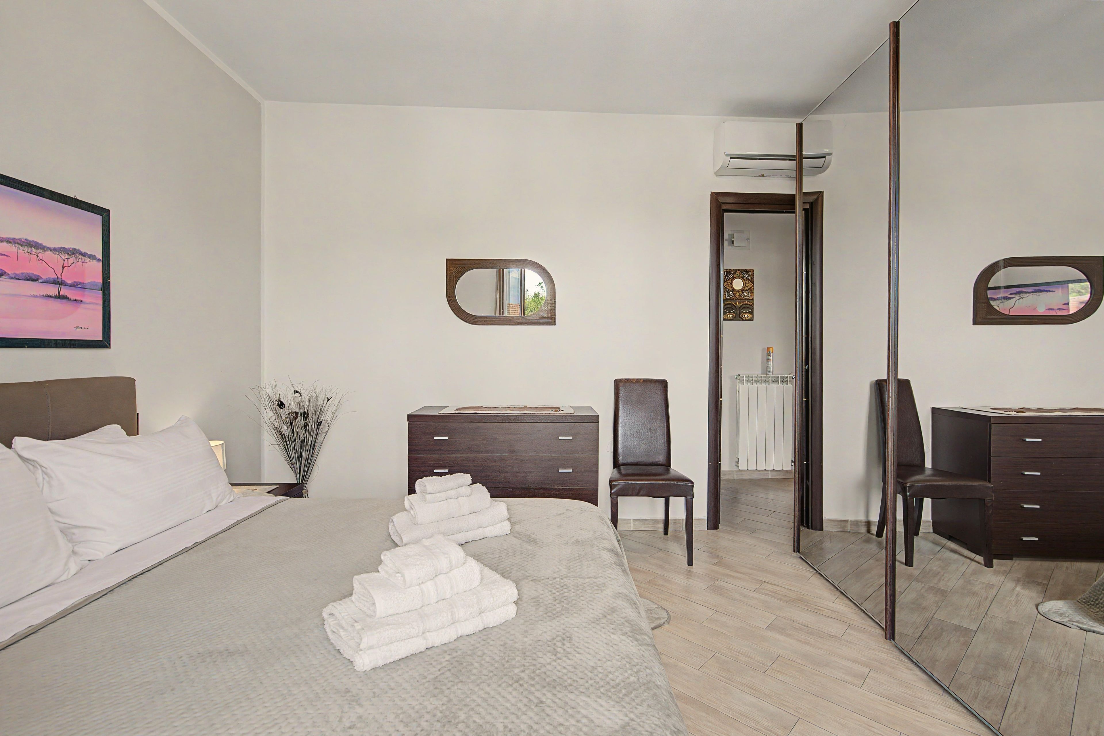 A bedroom with a bed, a dresser, a chair, a mirror, and a painting on the wall.