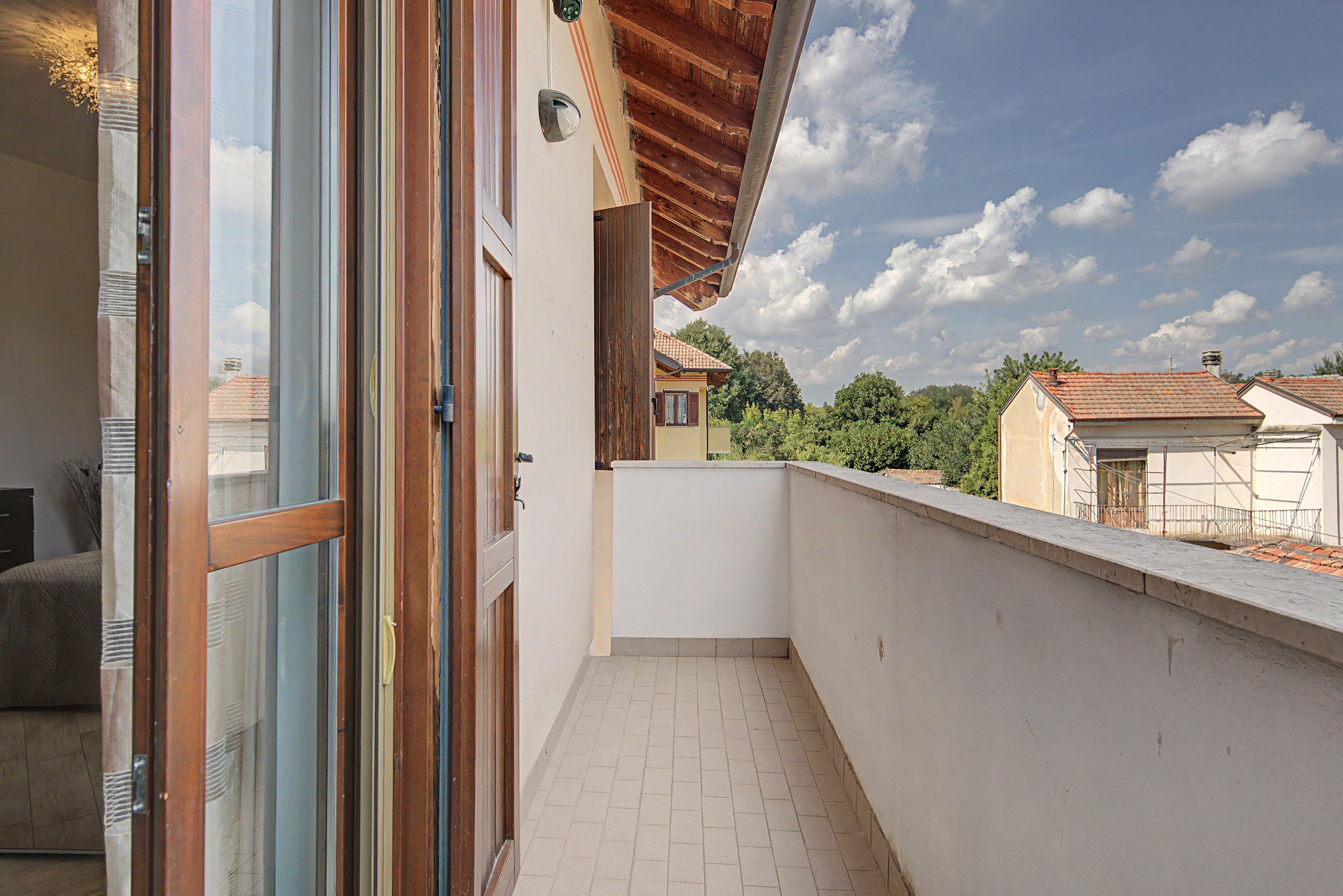 Un balcón con piso de baldosas, baranda de madera y vista a casas vecinas.