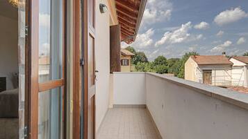 Un balcón con piso de baldosas, baranda de madera y vista a casas vecinas.