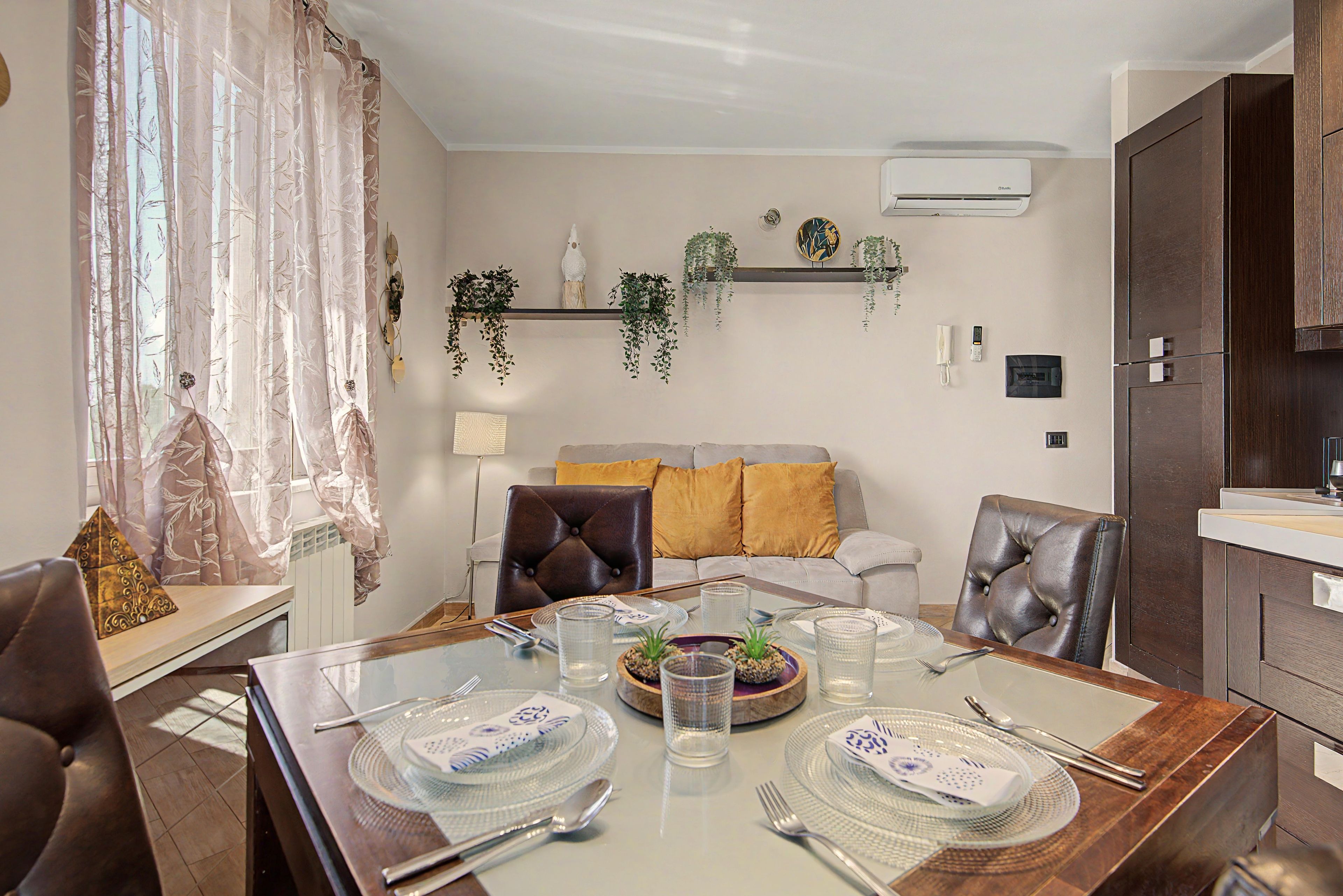 Un comedor con una mesa dispuesta para cuatro, un sofá con cojines y una estantería colgante para plantas.