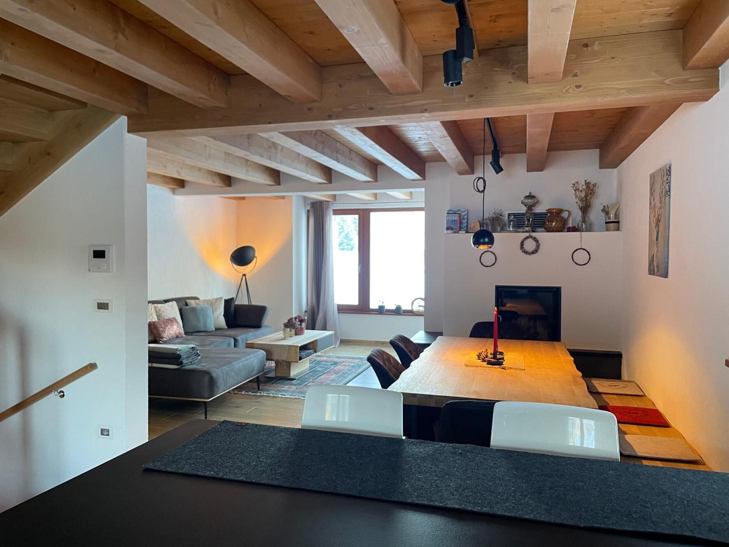 A modern interior with a wooden ceiling, a dining area with a long table, a sofa, and a floor lamp.