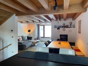 A modern interior with a wooden ceiling, a dining area with a long table, a sofa, and a floor lamp.