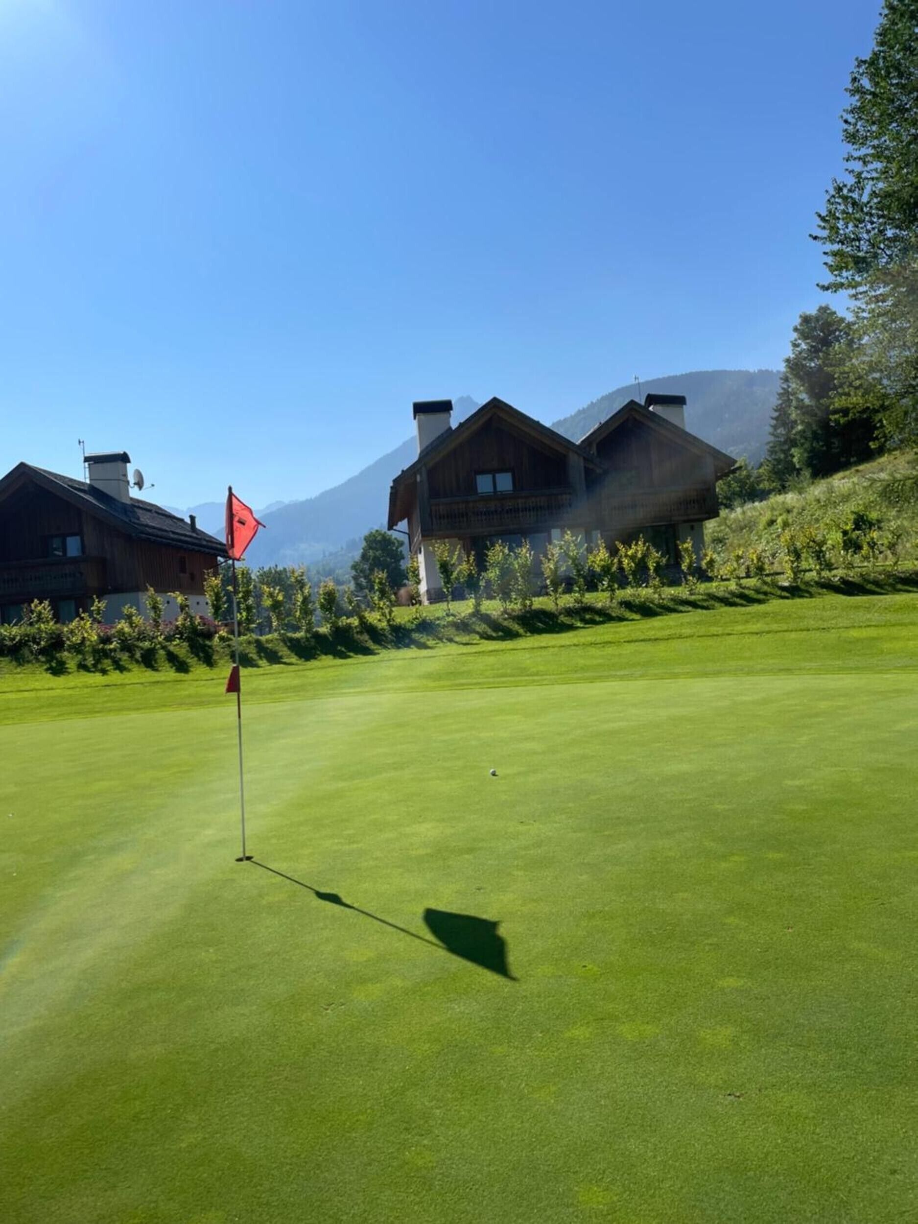 Ein Golfplatz mit Fahnenstange, einer roten Fahne und einem Gebäude im Hintergrund.