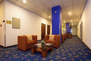Eine Hotelhalle mit Sitzbereichen, einer Rezeption und Hinweisschildern.