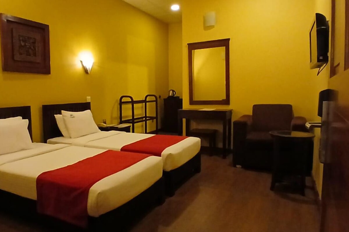 Ein Hotelzimmer mit zwei Betten, einem Schreibtisch, einem Sessel, einem Fernseher und einem Spiegel.