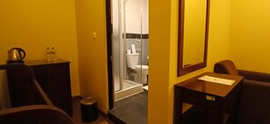 Ein Badezimmer in einem Hotel mit Dusche, Toilette und einem kleinen Tisch mit Papier darauf.