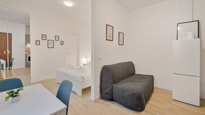 A modern, minimalistic room with a bed, a grey sofa, a white table with chairs, and a white refrigerator. - [Il Parco Apartment 6] Natura & Relax-RoadTo5Terre (Beverino)