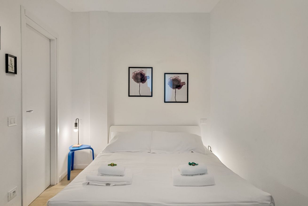 Ein Hotelzimmer mit einem Bett, zwei an der Wand befestigten Bildern, einem Nachttisch mit Lampe und einem blauen Sessel.