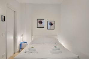 Ein Hotelzimmer mit einem Bett, zwei an der Wand befestigten Bildern, einem Nachttisch mit Lampe und einem blauen Sessel.
