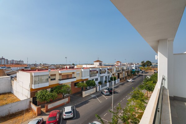 Une rue résidentielle bordée de voitures garées, des immeubles dotés de balcons et un ciel dégagé.