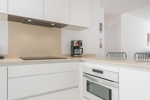 A modern kitchen with white cabinetry, a built-in oven, a coffee machine, and a radiator. - Apartamentos Puerto by H - Centro Ayamonte AEHP12CP104 (Ayamonte)