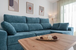 A teal sofa with a wooden coffee table in front, a floor lamp, and three abstract wall art pieces. - Apartamentos Puerto by H - Centro Ayamonte AEHP12CP104 (Ayamonte)