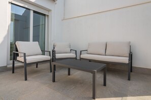 A patio area with a sofa set and a table, a sliding glass door, and a plain wall. - Apartamentos Puerto by H - Centro Ayamonte AEHP12CP104 (Ayamonte)