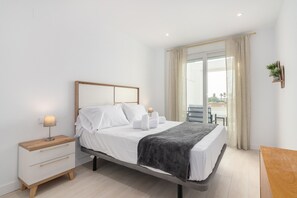 A modern hotel room with a bed, bedside tables, a small desk, and a view of the outdoors. - Apartamentos Puerto by H - Centro Ayamonte AEHP12CP104 (Ayamonte)