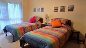 A room with two beds, each with colorful bedding, a nightstand with a lamp, and a small stool. - Homely - Queenscliff (QUEENSCLIFF)