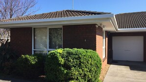 A residential house with a garage, a brick facade, and a well-maintained front yard. - Homely - Queenscliff (QUEENSCLIFF)