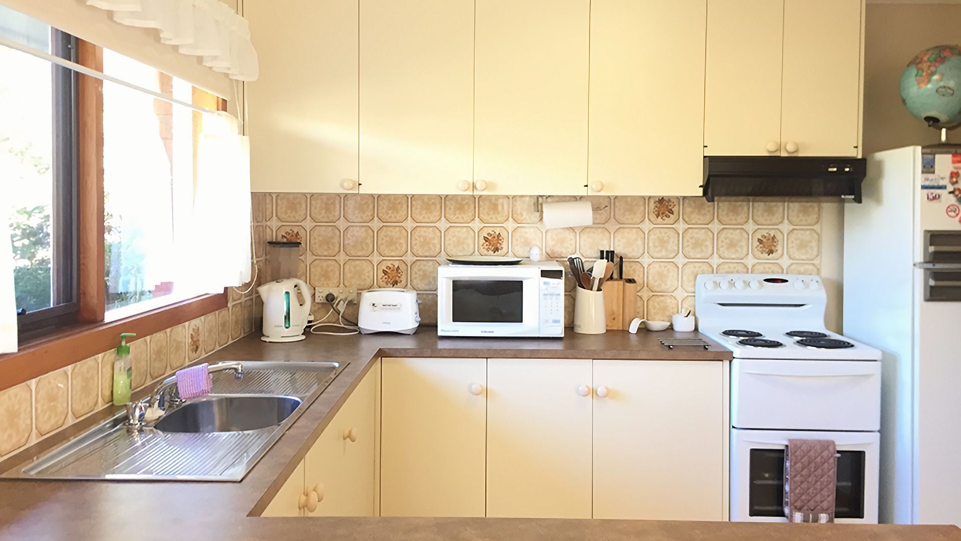 Eine kleine Küche mit Spüle, Mikrowelle, Toaster, Herd und einem Fenster mit Vorhängen.