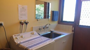 A compact laundry area with a washing machine, a sink, and a mirror. - Homely - Queenscliff (QUEENSCLIFF)