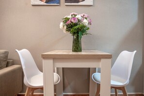 A dining table with a vase of flowers, two white chairs, and a beige wall with two framed pictures. - Cozy and lovely apartment located in the historic center of Málaga. (Málaga)