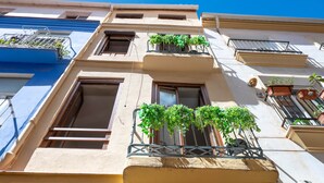Un edificio de varios pisos con balcones, algunos con plantas, y un cielo azul despejado.