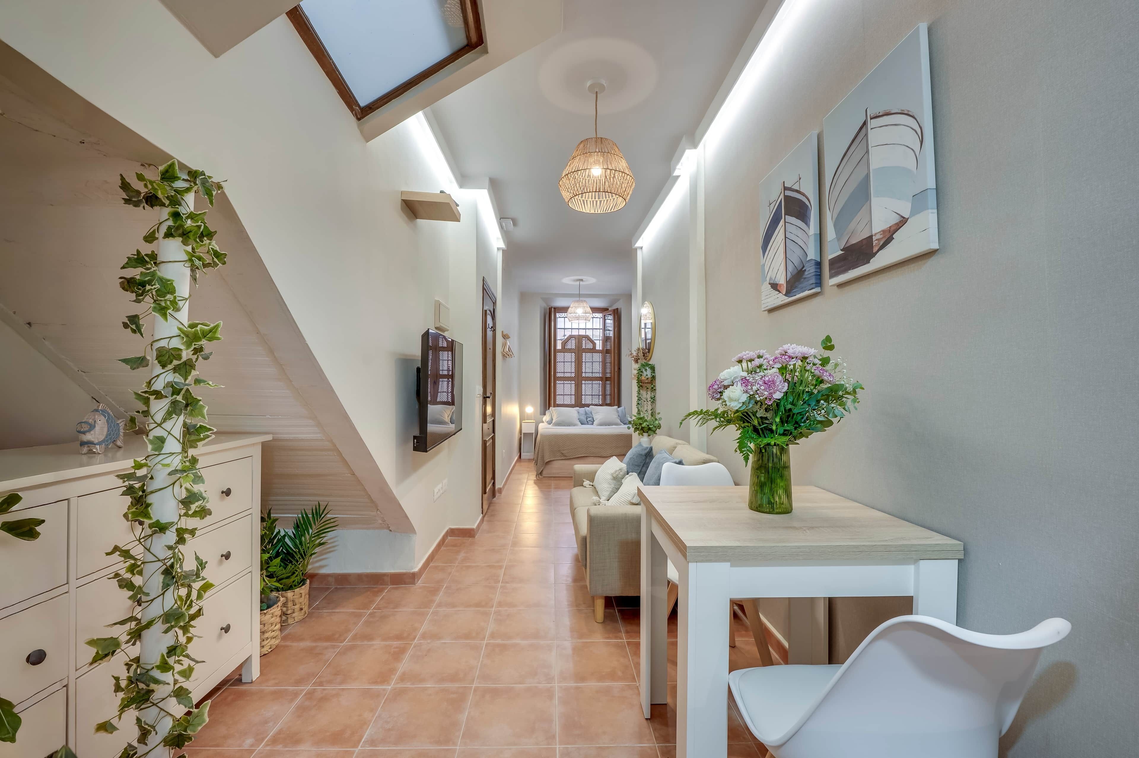 A hallway with a staircase, a dining area with a table and chairs, and a bed in the background.