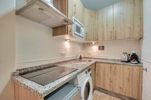 A compact kitchen with wooden cabinets, a built-in microwave, a stainless steel sink, and a washing machine. - Cozy and lovely apartment located in the historic center of Málaga. (Málaga)