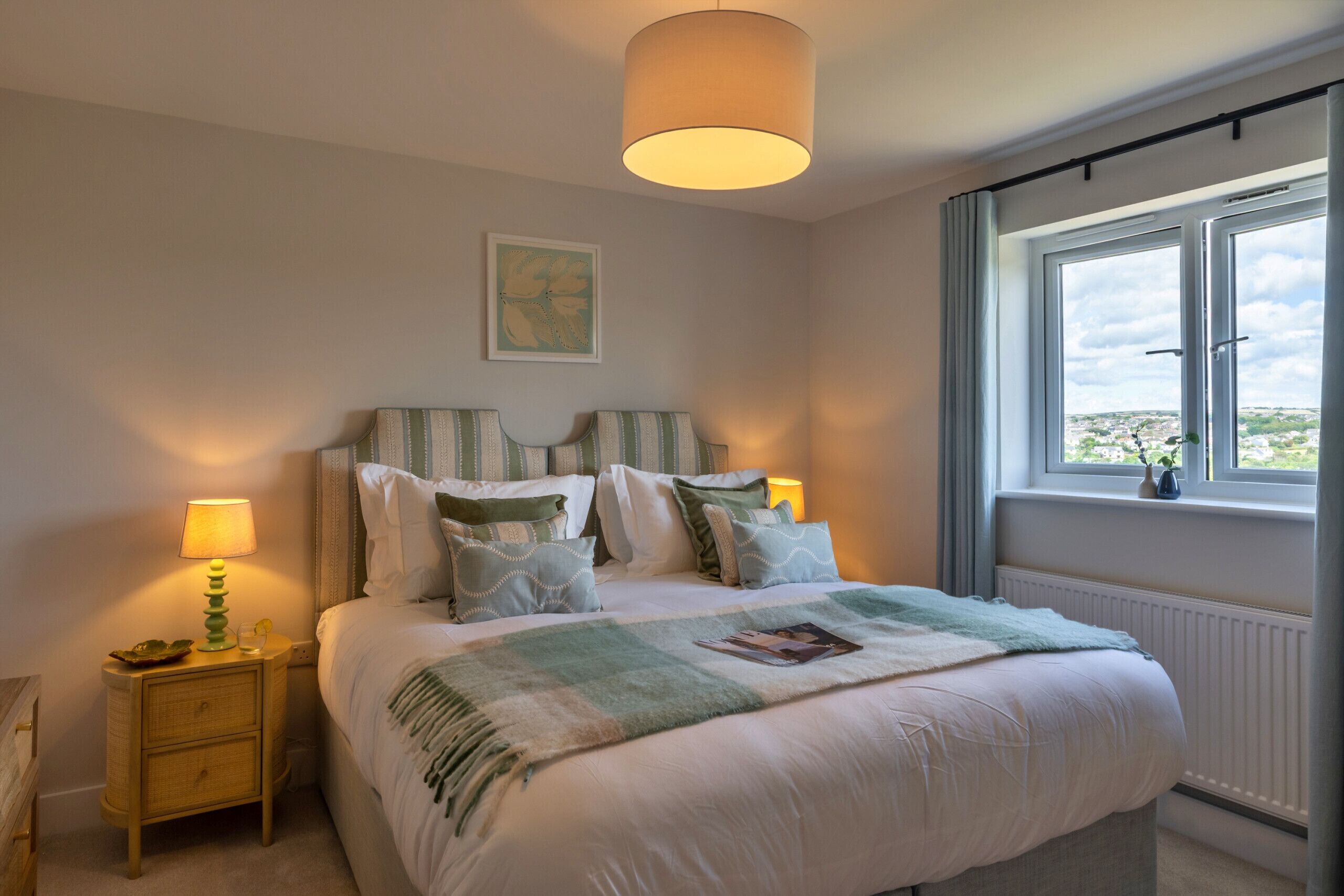 A bedroom with a bed, bedside lamps, a window with a view, and a wall-mounted artwork.