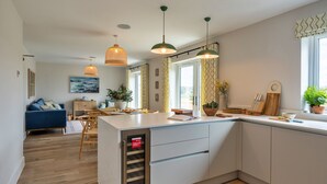 Une cuisine moderne dotée d’un îlot central, de planchers en bois, de luminaires suspendus et offrant une vue sur l’espace de vie.