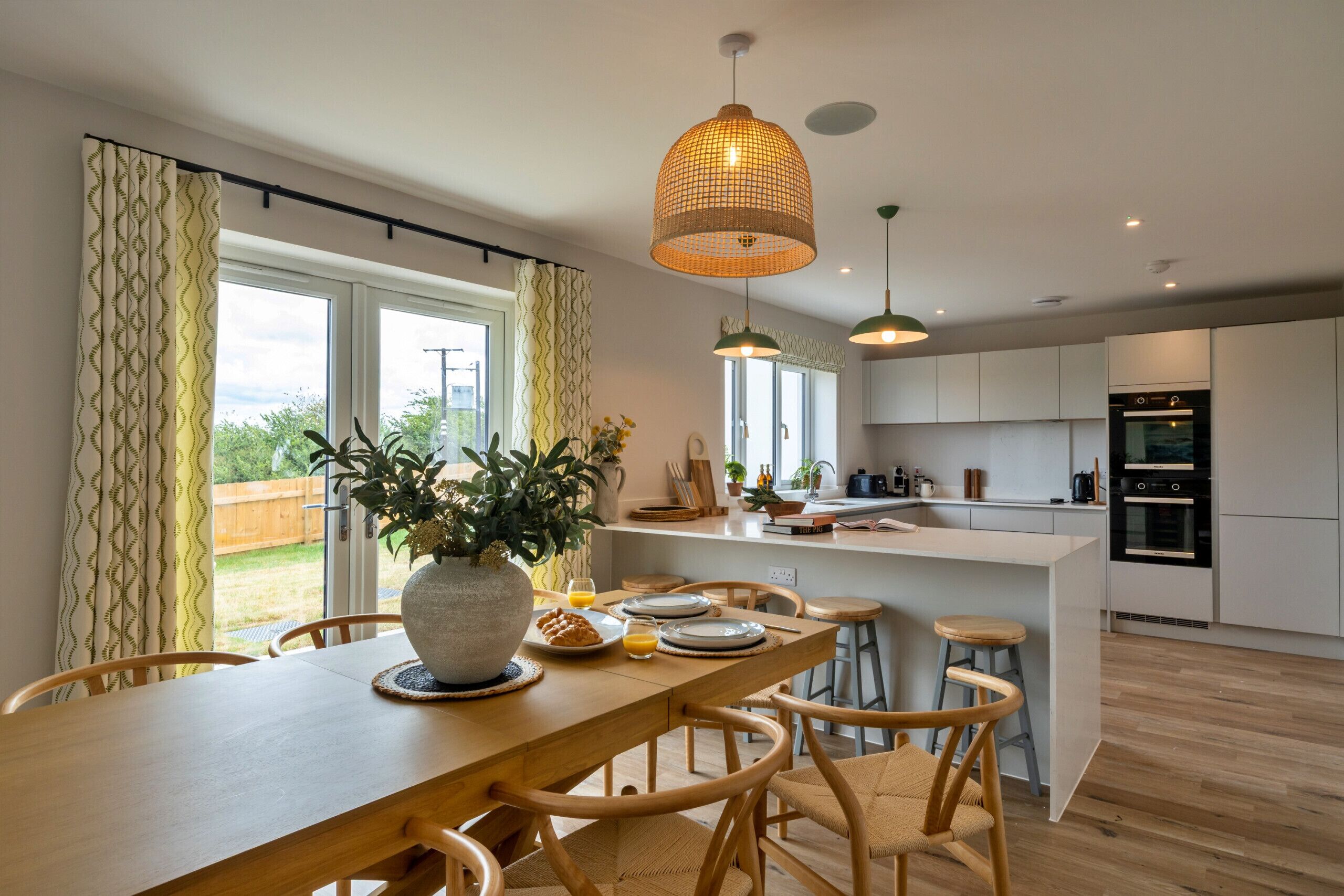 A modern kitchen with a central island, wooden chairs, and pendant lighting.